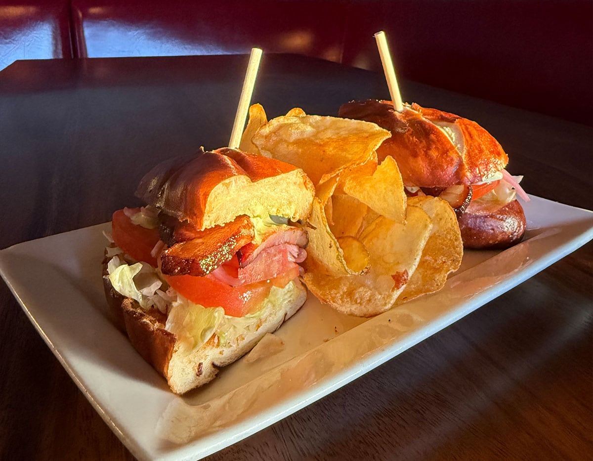 A ham sandwich on a brioche bun with chips